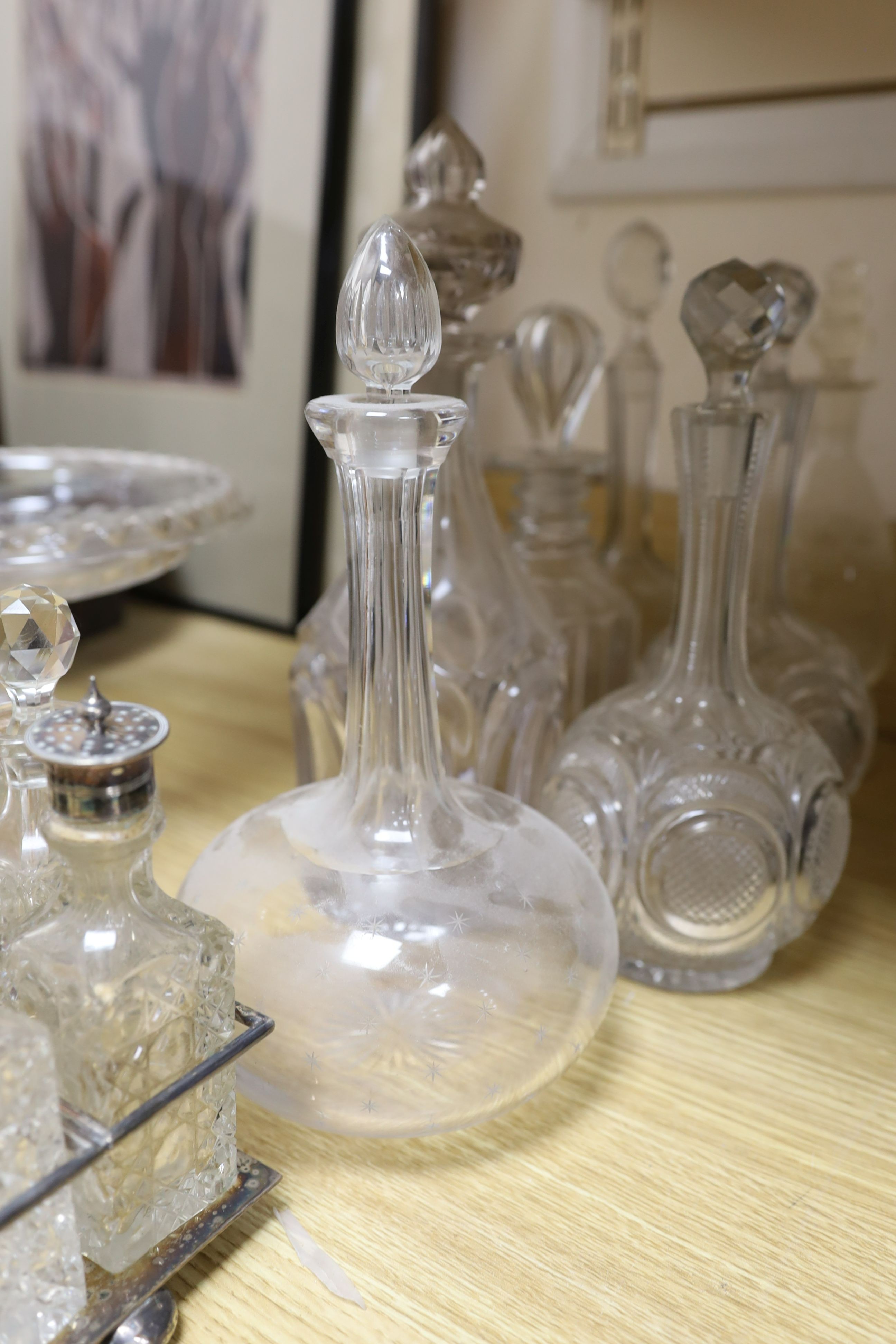 Sundry glassware including a six bottle cruet set on a plated stand, a Victorian cut glass jug, a pair of long neck decanters, five other decanters and a glass cake tazza